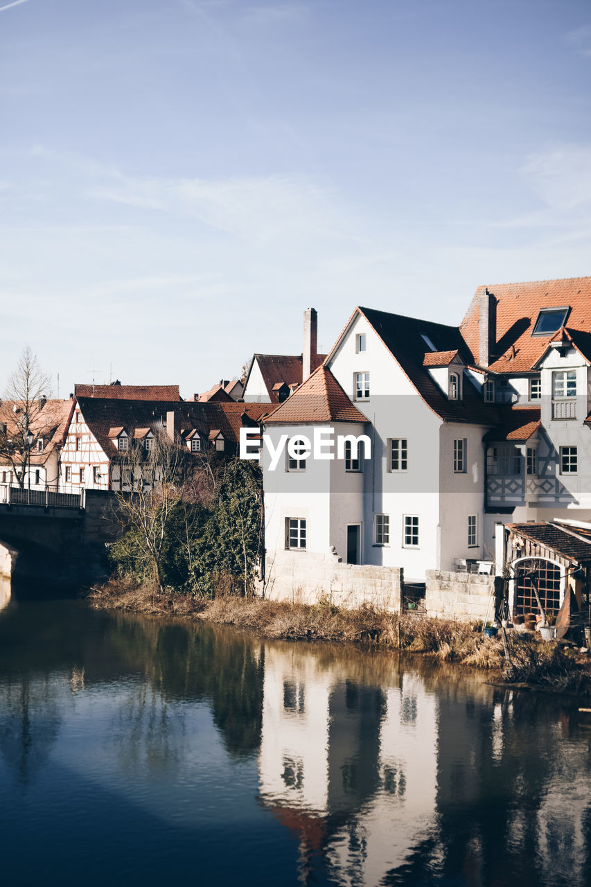 Houses by river and buildings in town against sky