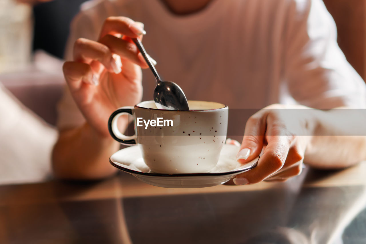 Closeup of female hands with french manicure holding cozy ceramic white mug of tea or coffee. relax