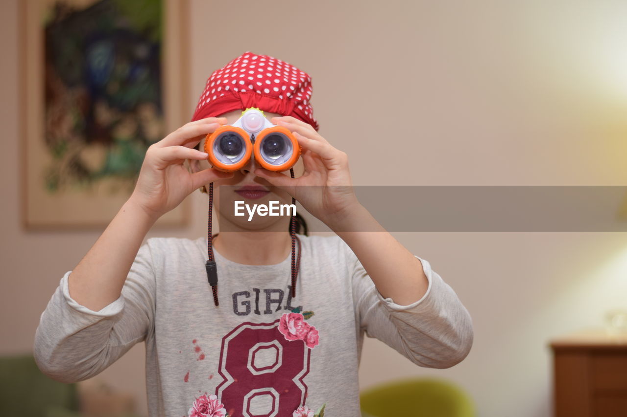 Girl looking through binoculars against wall