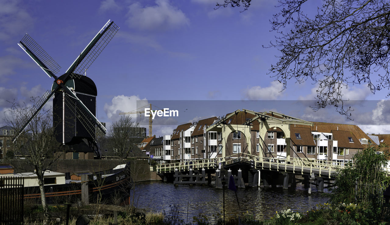 architecture, renewable energy, windmill, alternative energy, sky, built structure, environmental conservation, mill, building, water, nature, wind power, power generation, wind turbine, turbine, environment, building exterior, cloud, traditional windmill, no people, tree, plant, day, travel destinations, outdoors, waterway, lake, landmark, town, history, urban area, the past