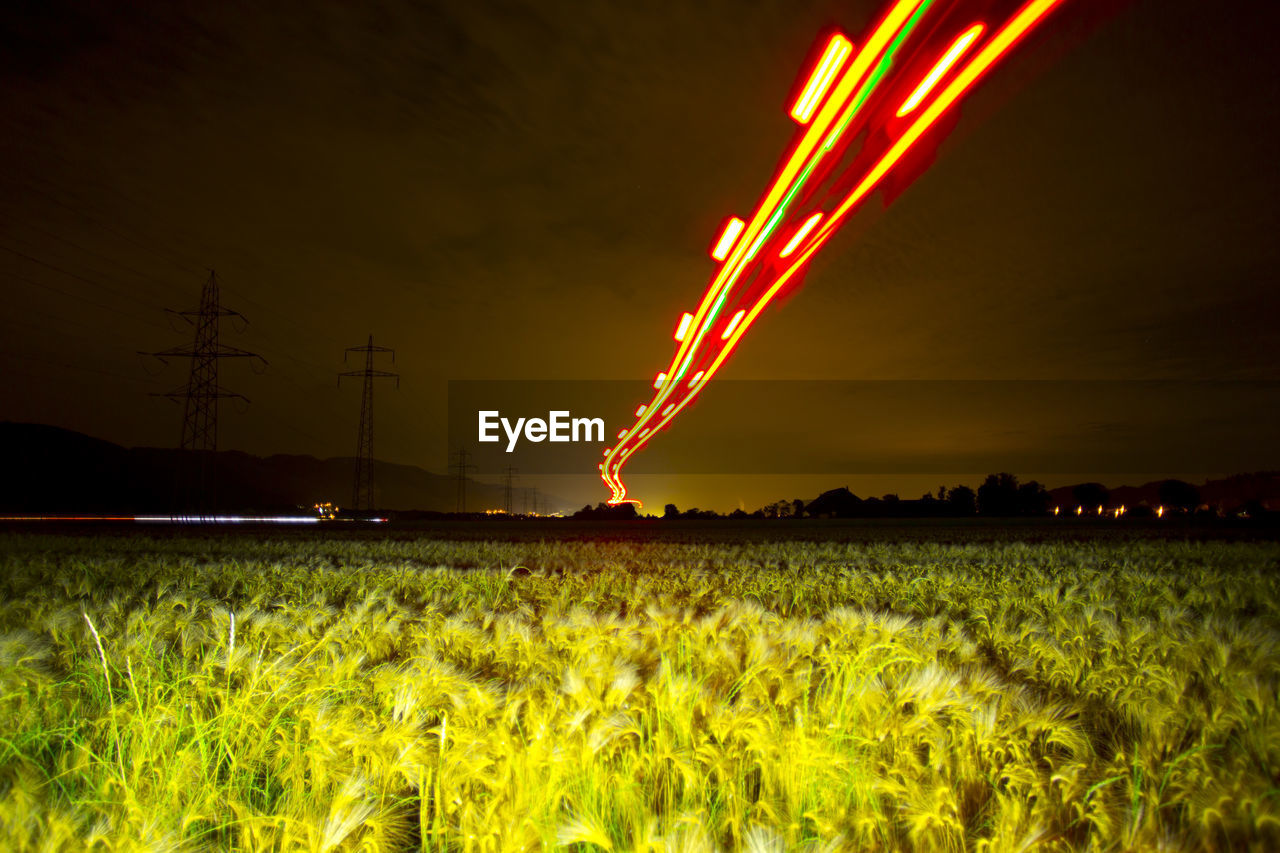 Low angle view of red light trails over field against sky at night