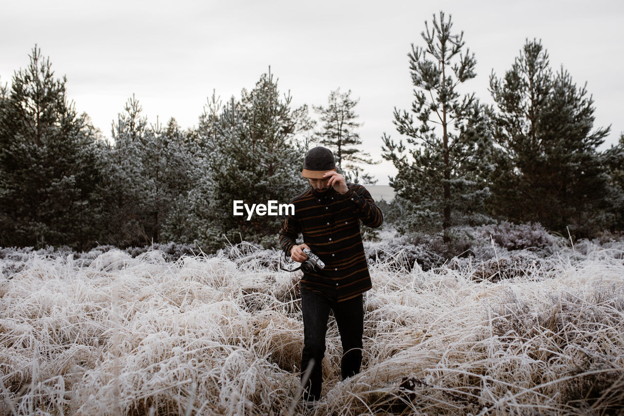 Man with photo camera standing in meadow with frozen grass in winter in scottish highlands