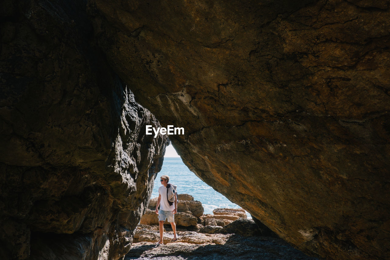 Man seen through cave standing at beach