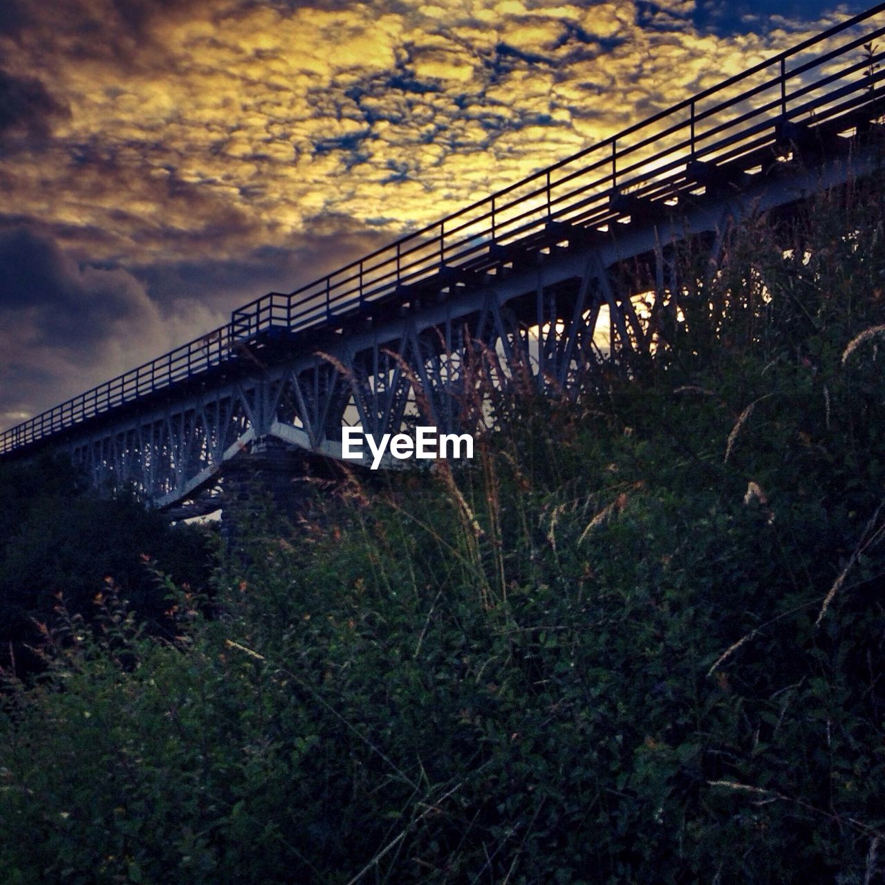 Low angle view of bridge over field against cloudy sky