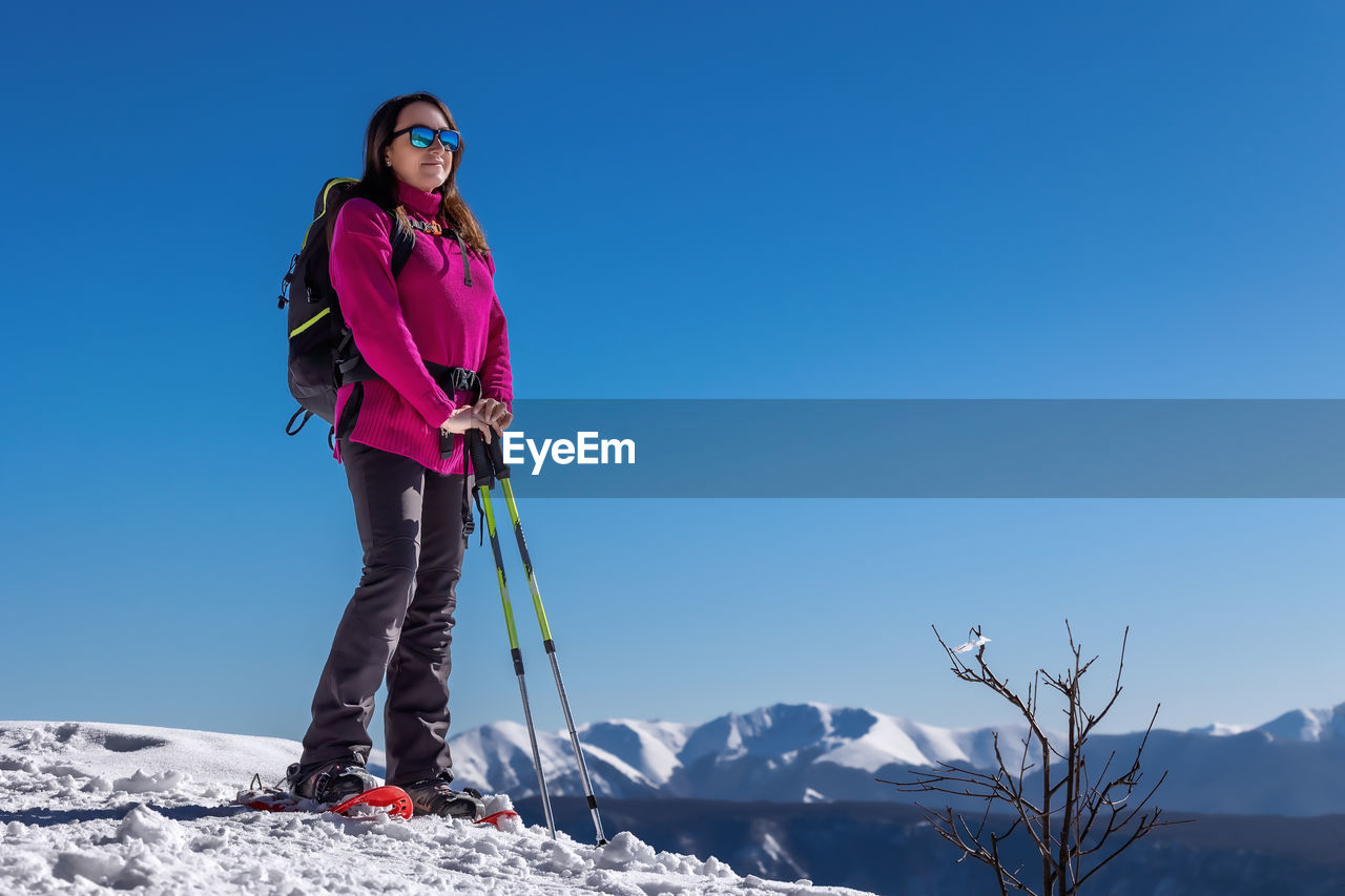 Snow hiker in the mountains, with snowshoes, snow poles and backpack. middle-aged woman, full length