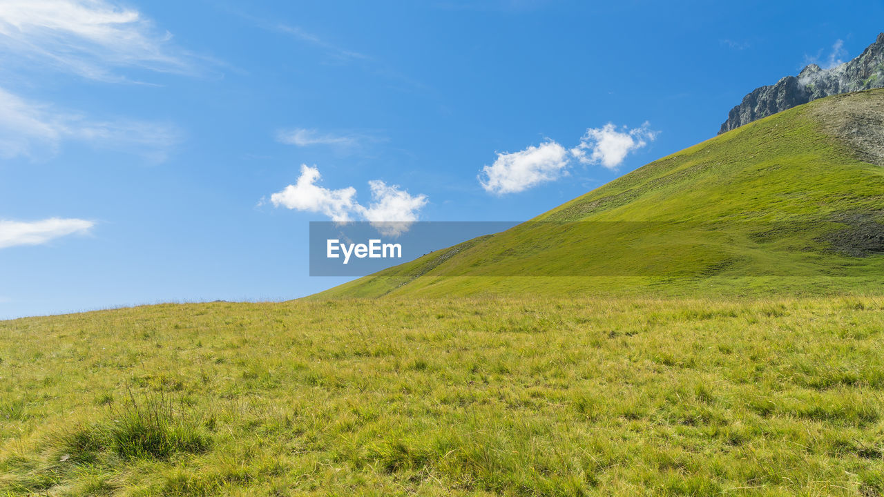 Low angle view of green landscape against blue sky