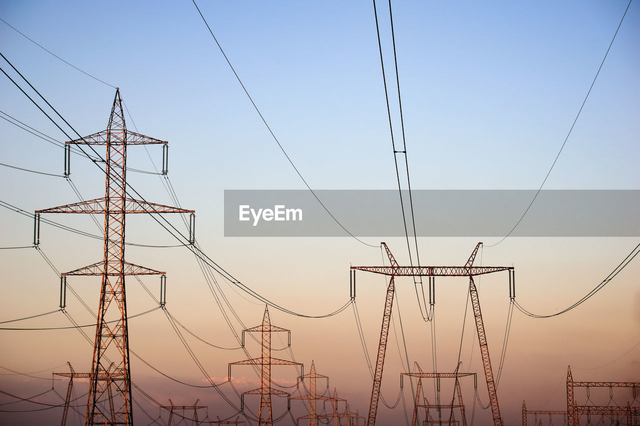 Electricity pylons against sky at sunset