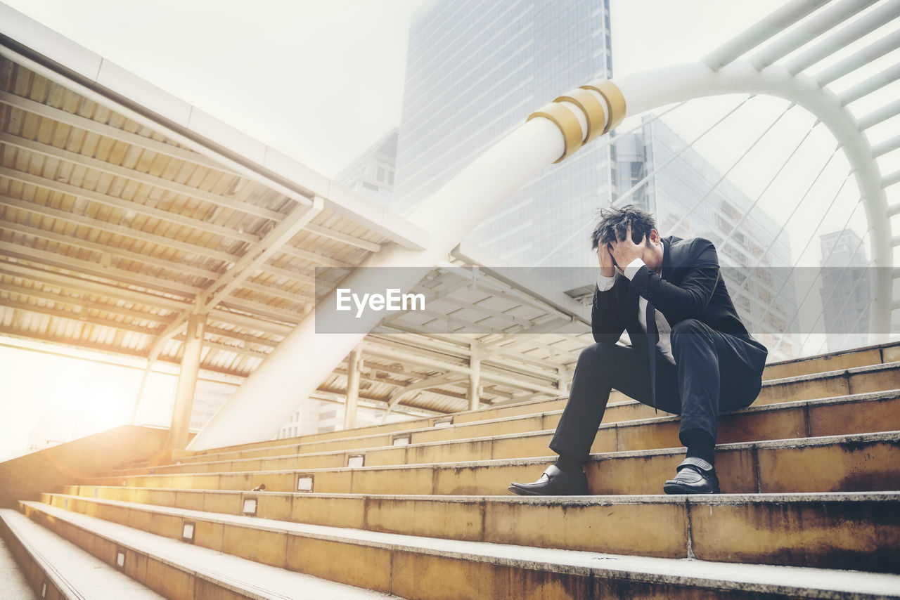 Full length of stressed businessman sitting on staircase in city