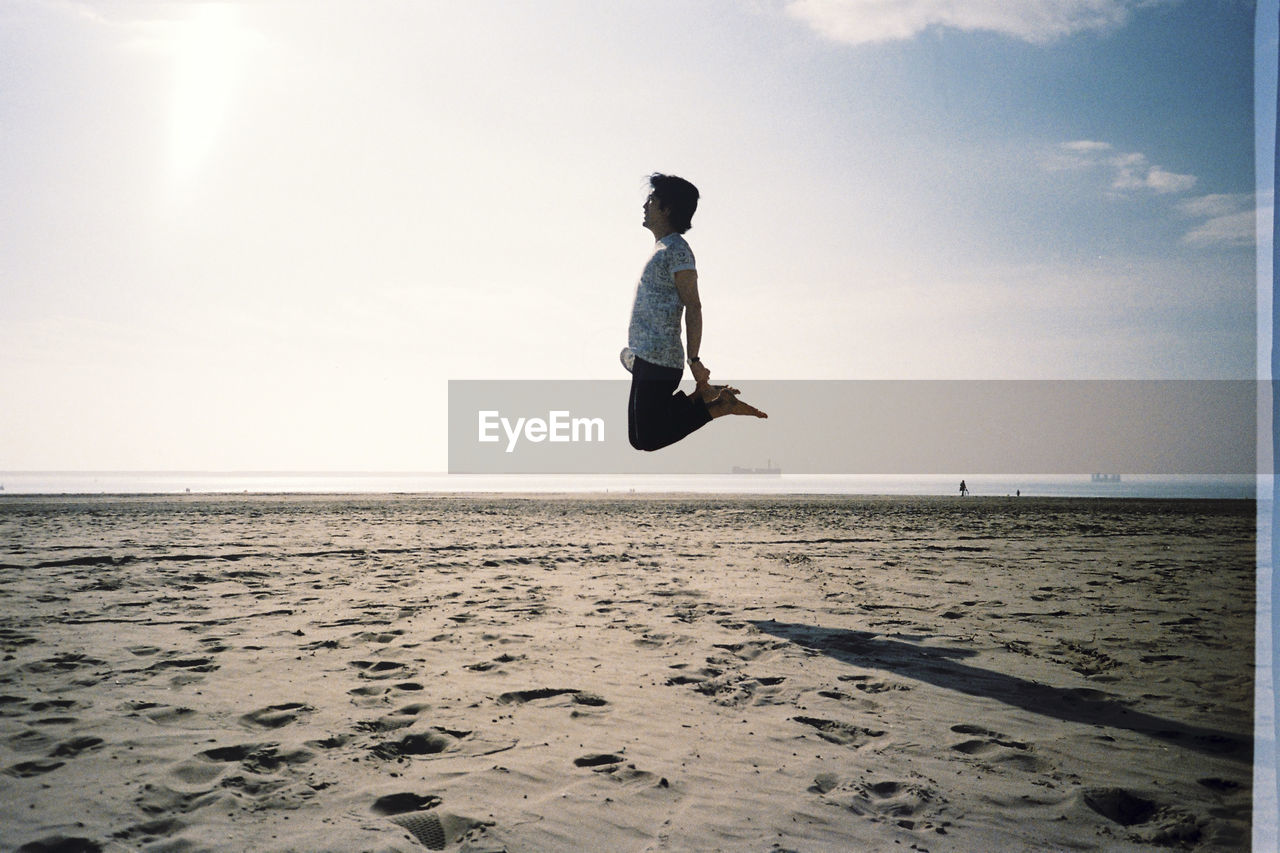 Man levitating at beach against sky