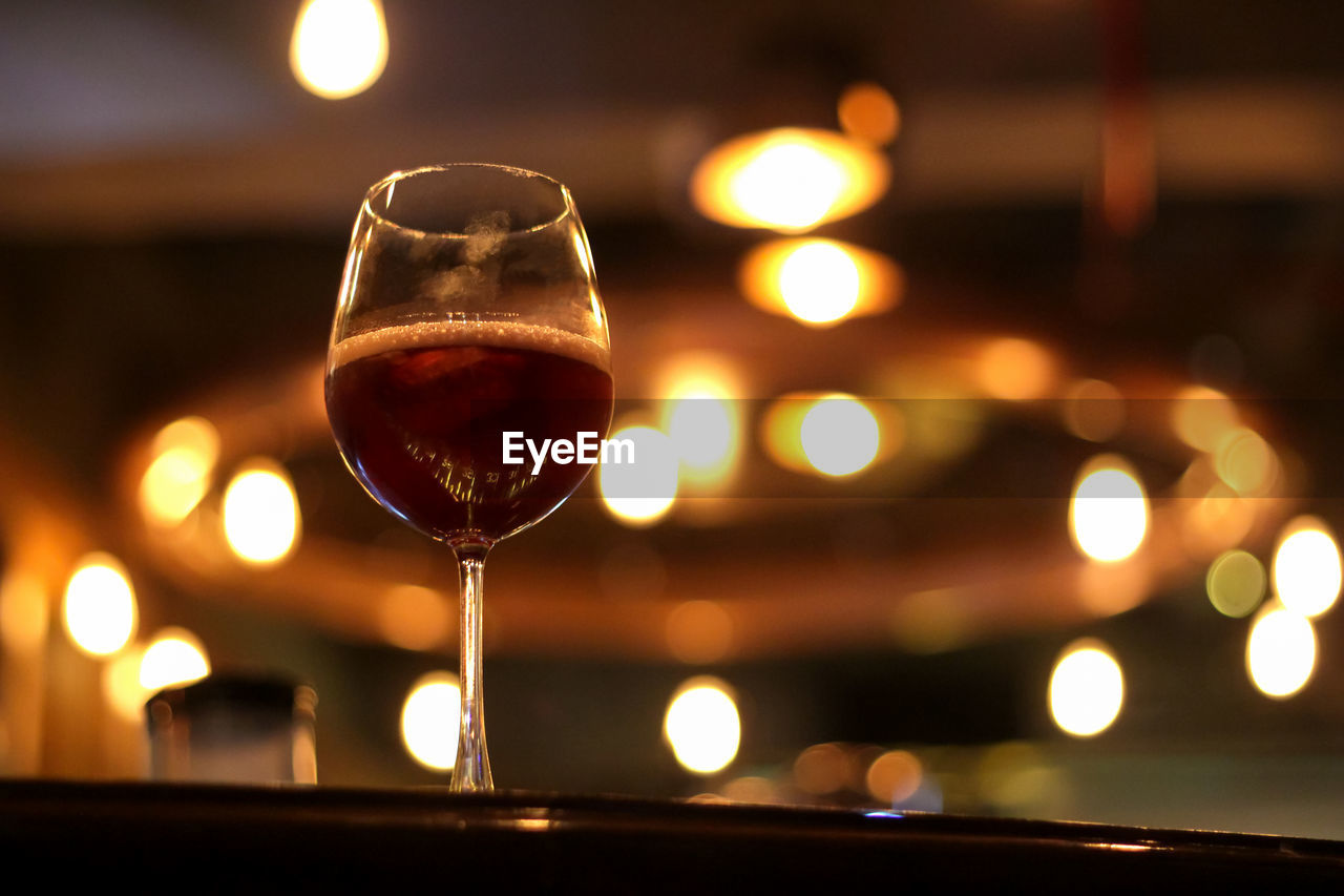 CLOSE-UP OF WINE GLASS AGAINST ILLUMINATED LIGHTS