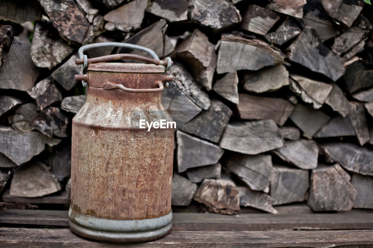 Old rusty milk can with background of chopped wood. close-up of old can on table against wooden wall