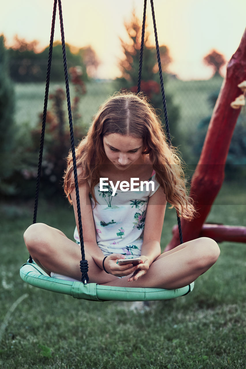 Girl using mobile phone while sitting on swing