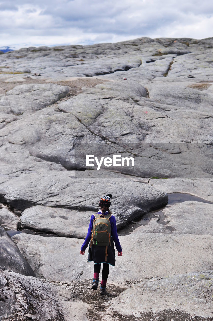 Rear view of backpack woman walking on rock formation