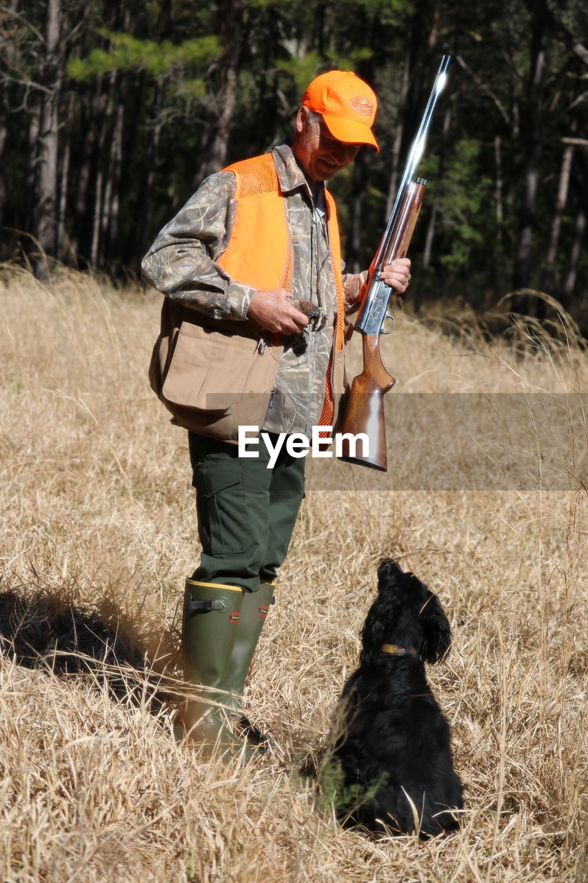 Man holding shotgun while standing by dog on grassy field