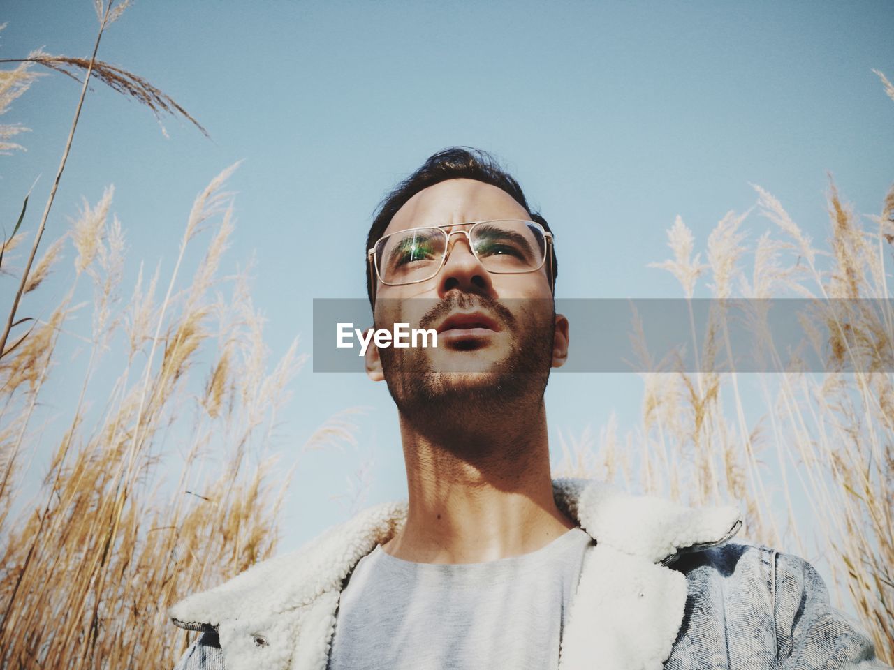 Young man wearing eyeglasses while standing by plants against sky