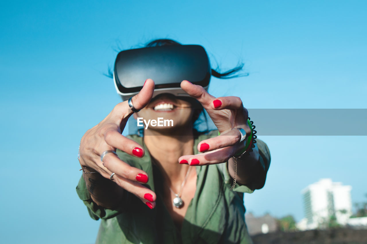 Low angle view of woman using virtual reality simulator against sky