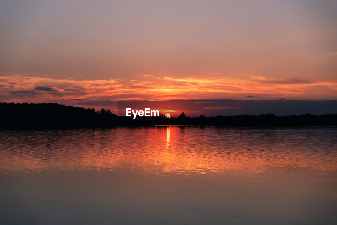 Sun setting behind the trees on horizon of a lake in ontario, canada.