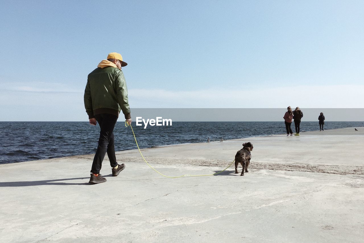 REAR VIEW OF PEOPLE WALKING AT BEACH AGAINST SKY