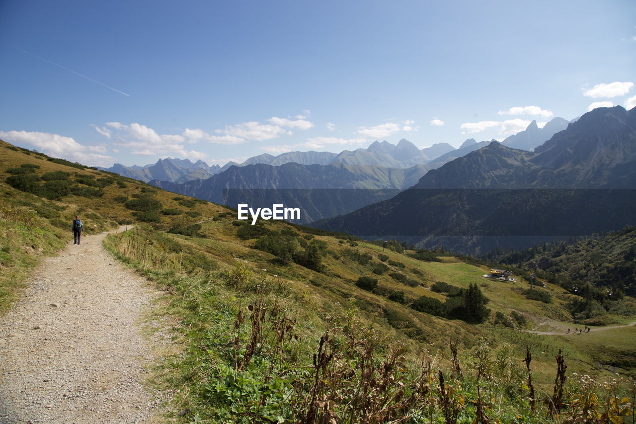 Rear view of man walking on the path by mountain against cloudy sky