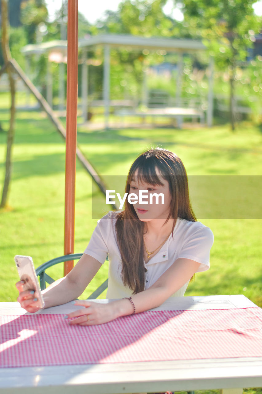 portrait of young woman using mobile phone while sitting at park