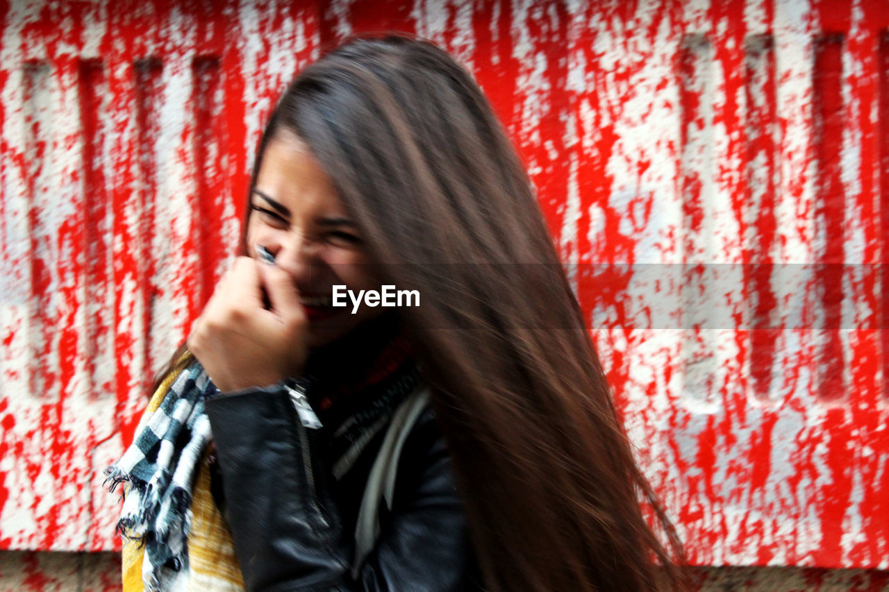 Close-up of young woman laughing while standing against weathered wall