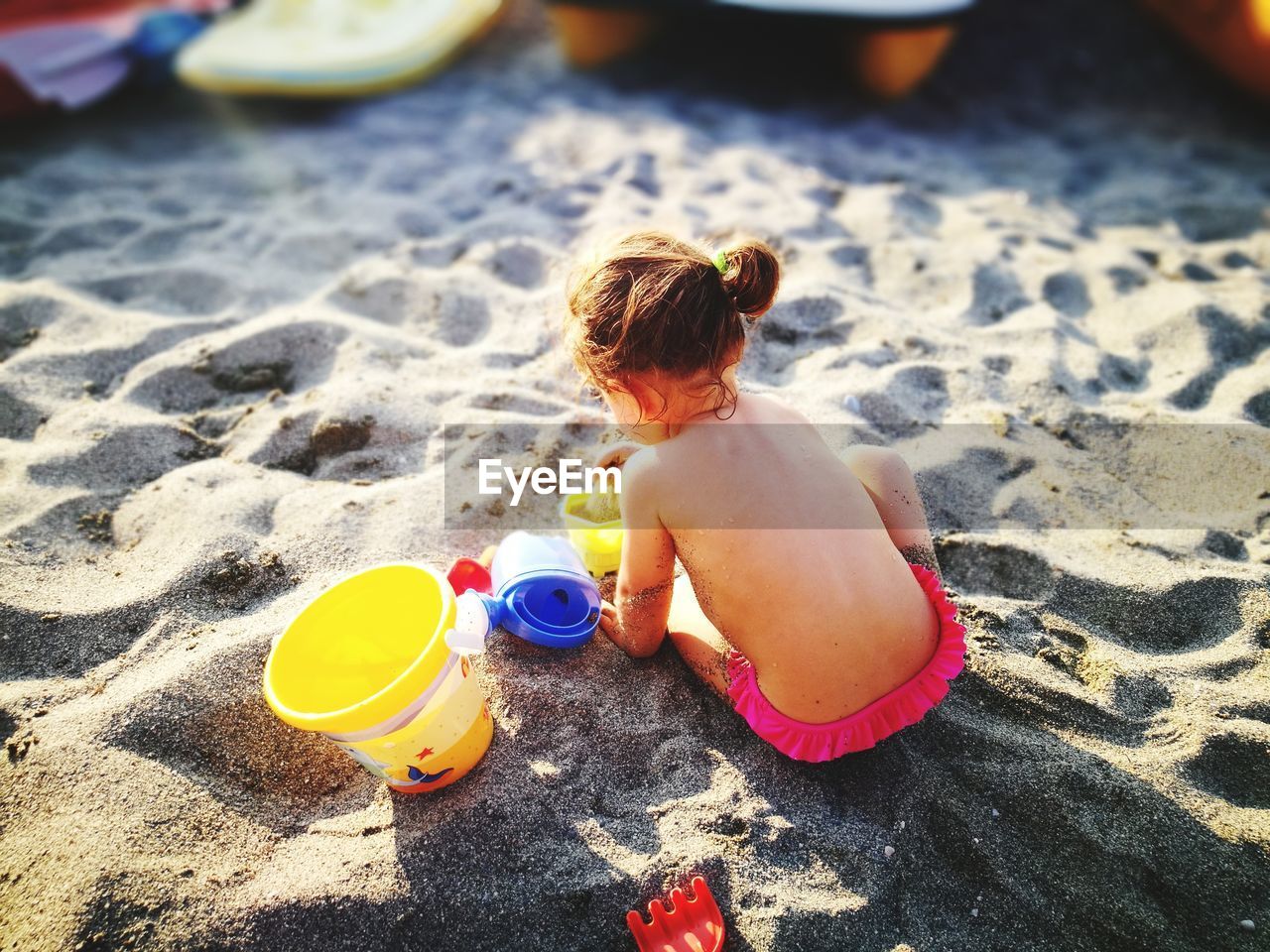 Rear view of shirtless baby girl playing with sand at beach