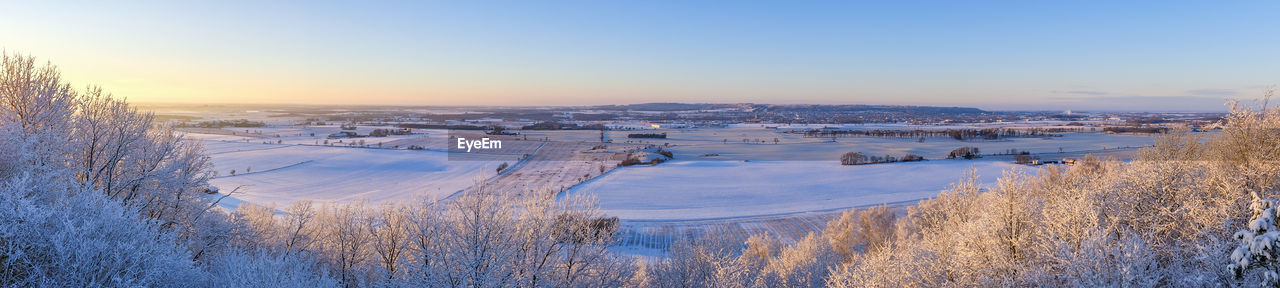 Panoramic view of snow covered land against sky during sunset