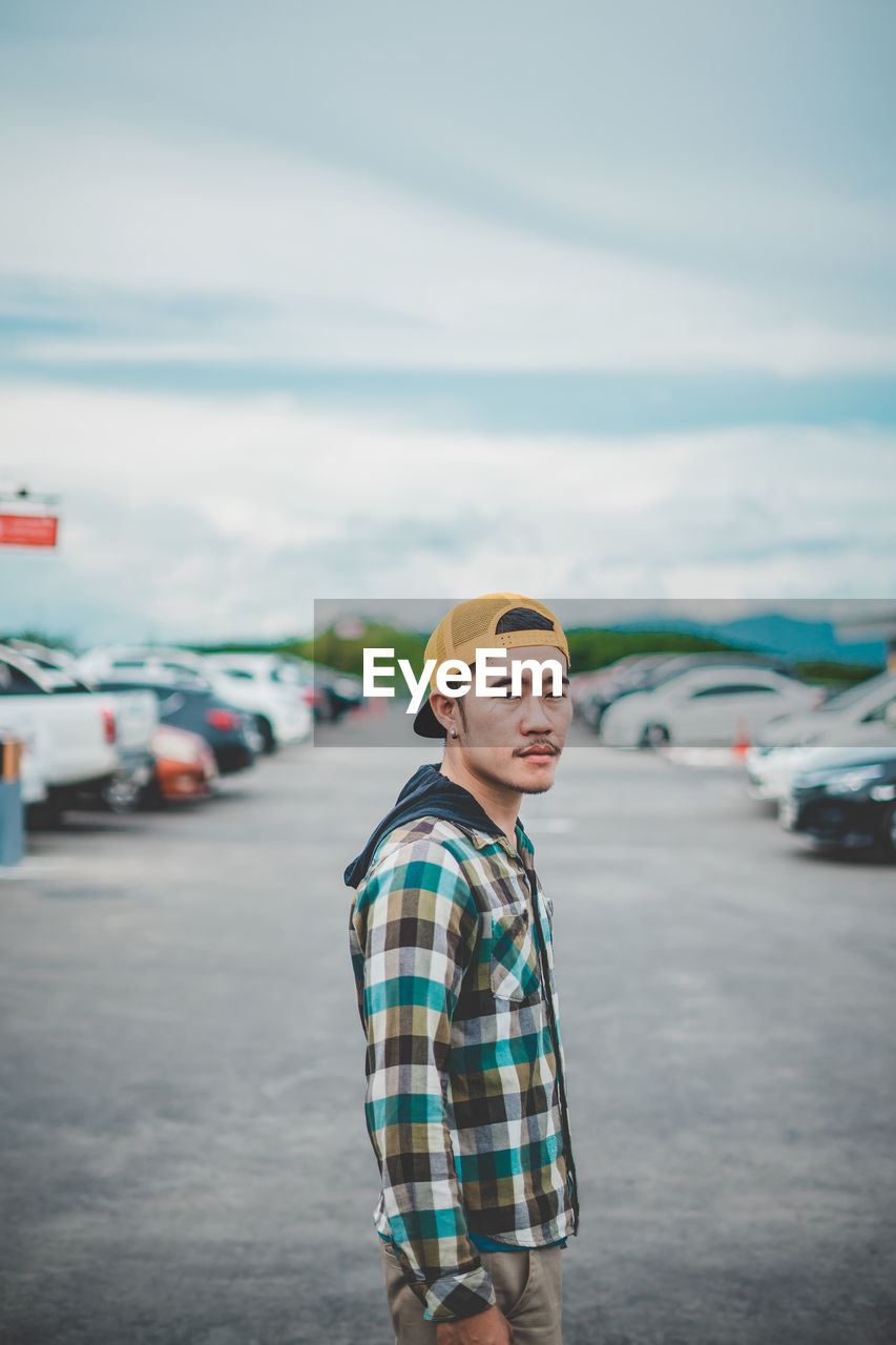 Side view portrait of young man standing on street against sky