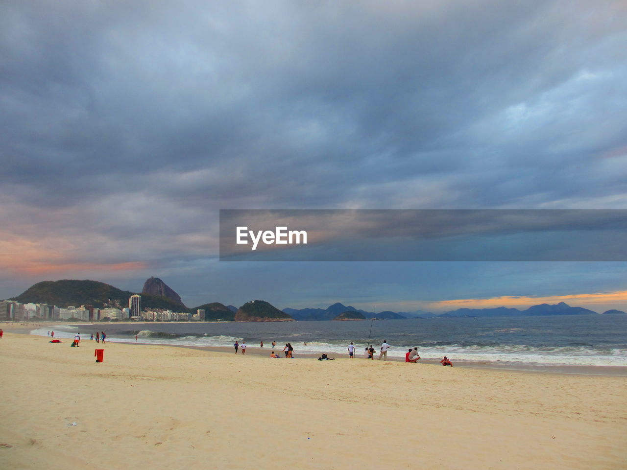 Tourists on beach against cloudy sky