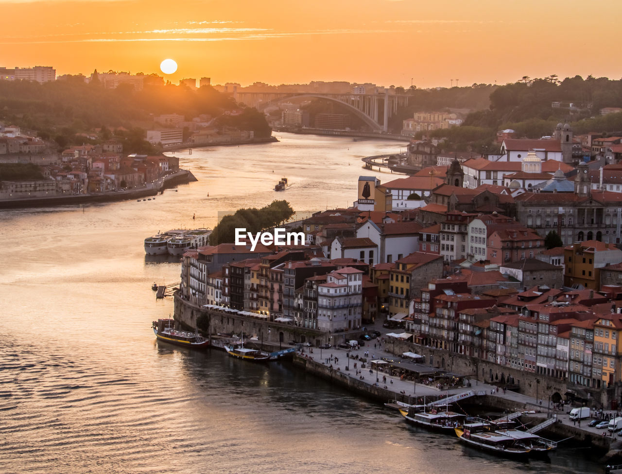 Boats moored in sea by city against sky during sunset