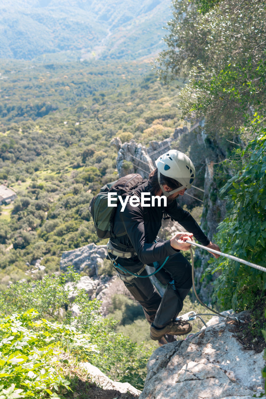 Adventure. man with helmet, harness and backpack. descending in the mountains by a via ferrata.