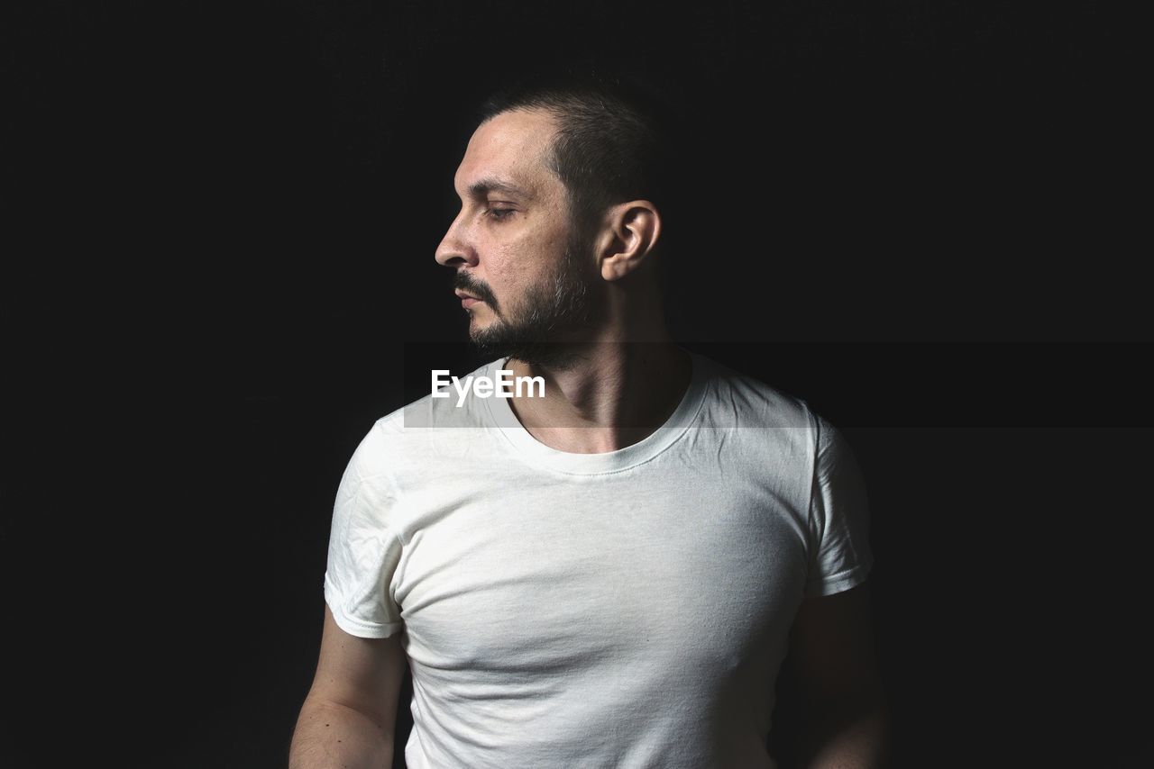 Portrait of young man looking away against black background