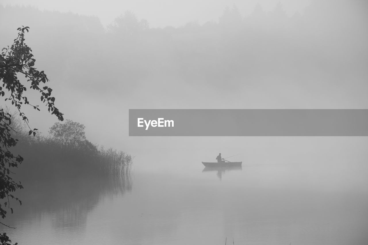 Silhouette person riding boat on lake in foggy weather