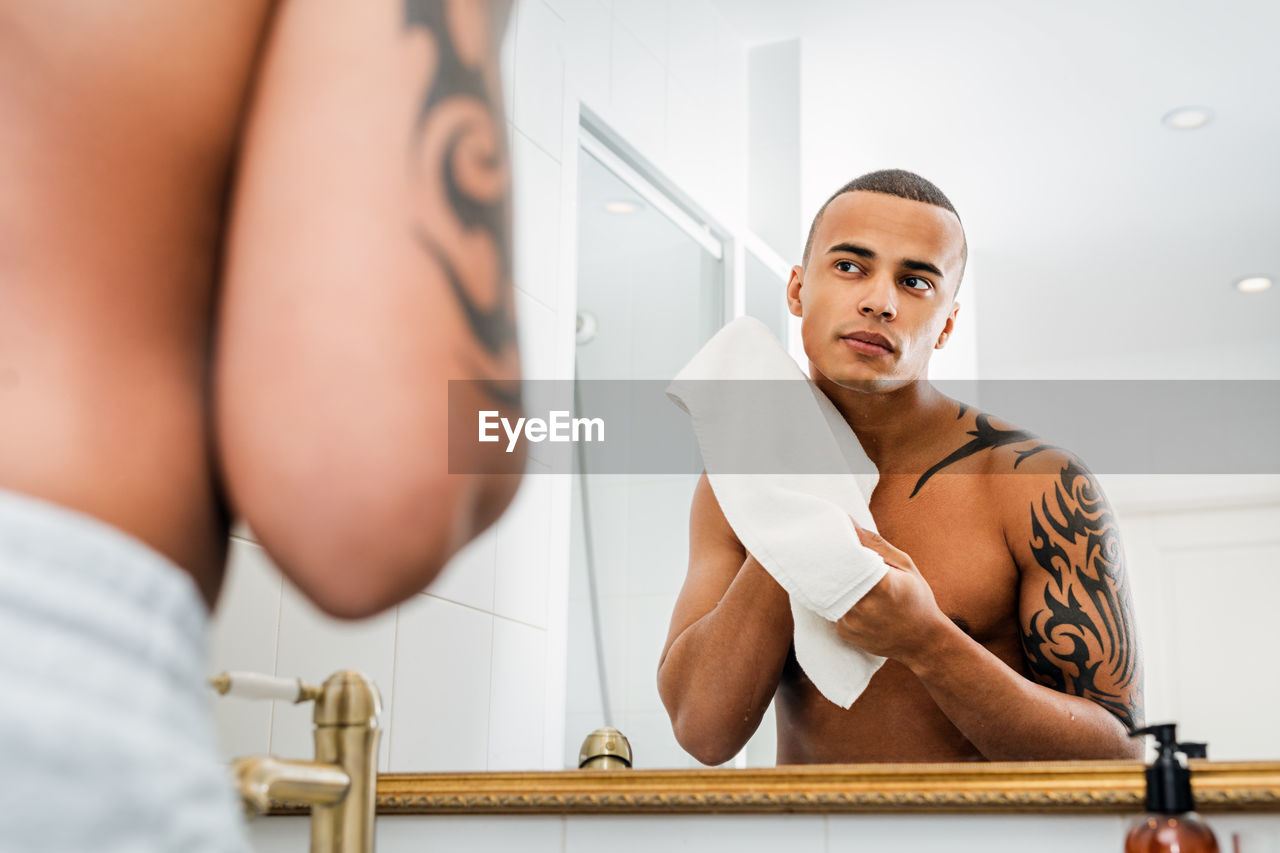 Young man holding towel looking at reflection in mirror at home