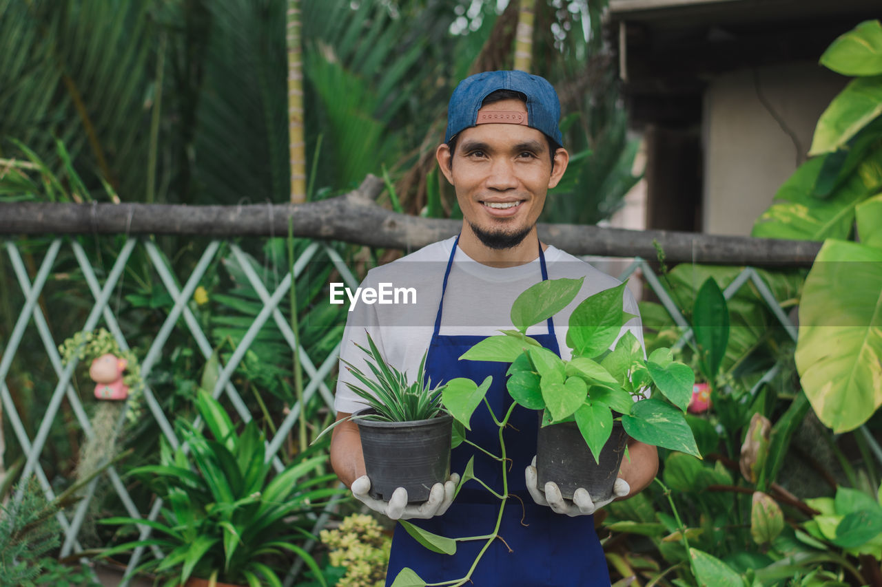 Portrait of smiling botanist holding plant at shop