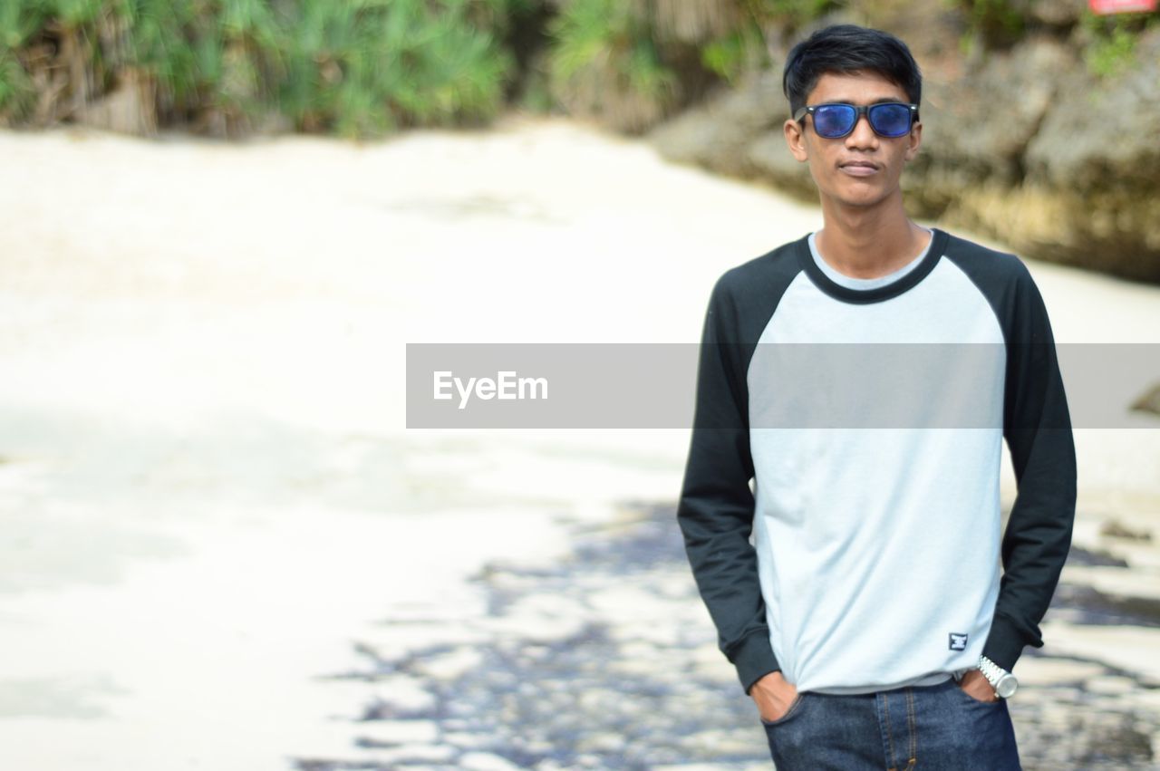 Portrait of young man wearing sunglasses while standing at beach