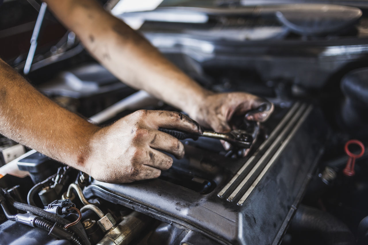 Unrecognizable technician with greasy hands turning screw with spanner while fixing engine of car in garage