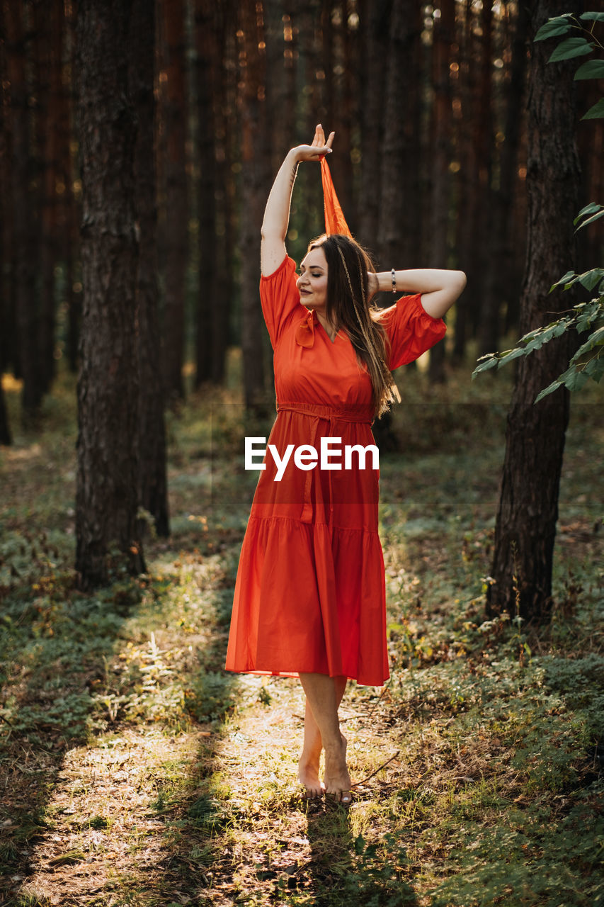 Alone woman in red dress dance on sun pine forest nature background