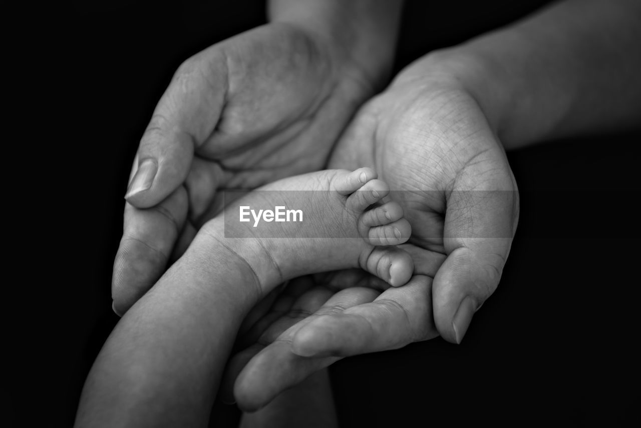 Close-up of father holding baby foot against black background