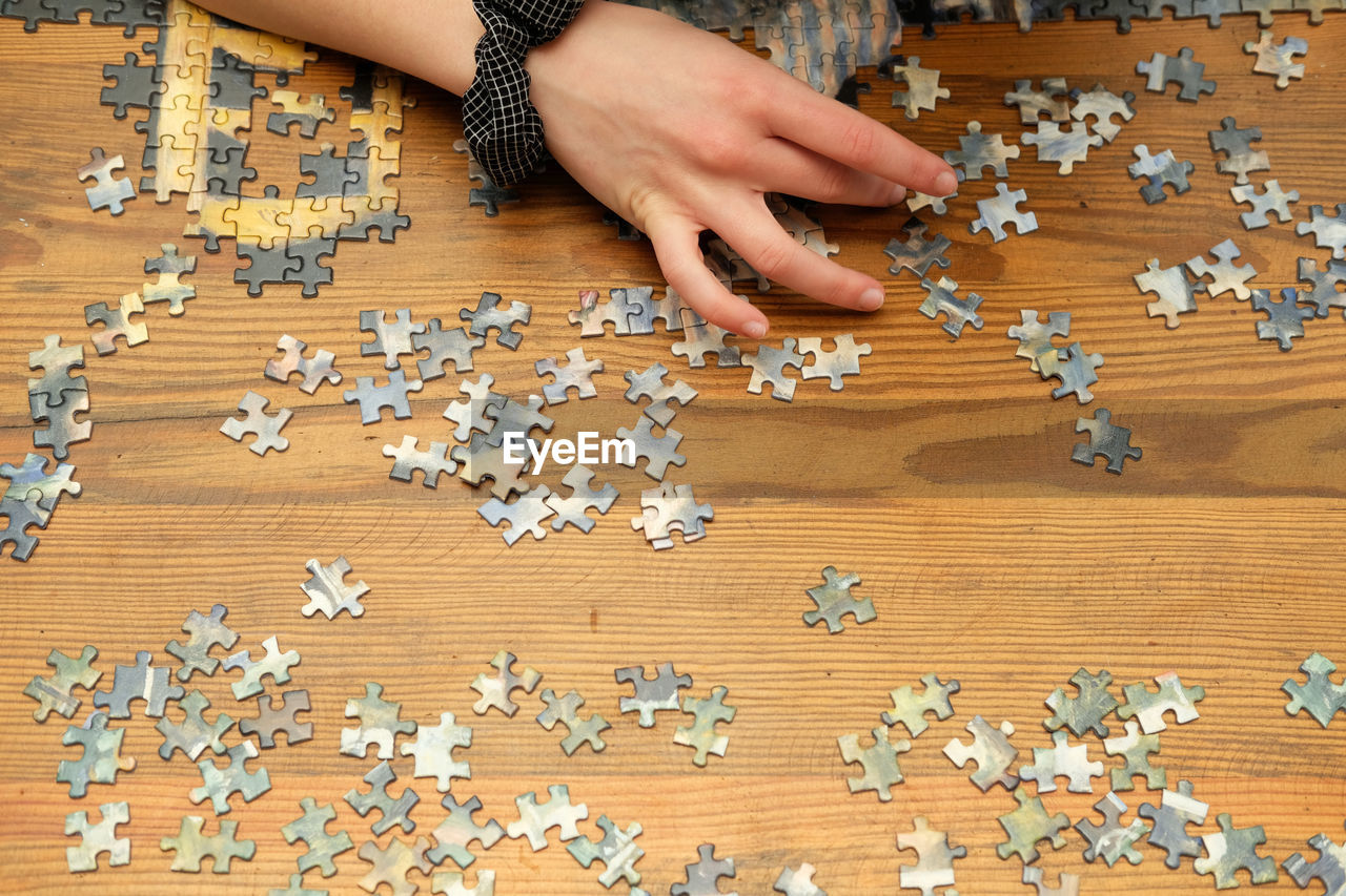 hand, indoors, one person, flooring, large group of objects, jigsaw piece, jigsaw puzzle, floor, pattern, wood, adult, puzzle, table, high angle view, women, game, abundance, bead