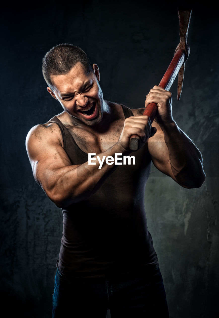 Aggressive muscular man holding pick axe against wall