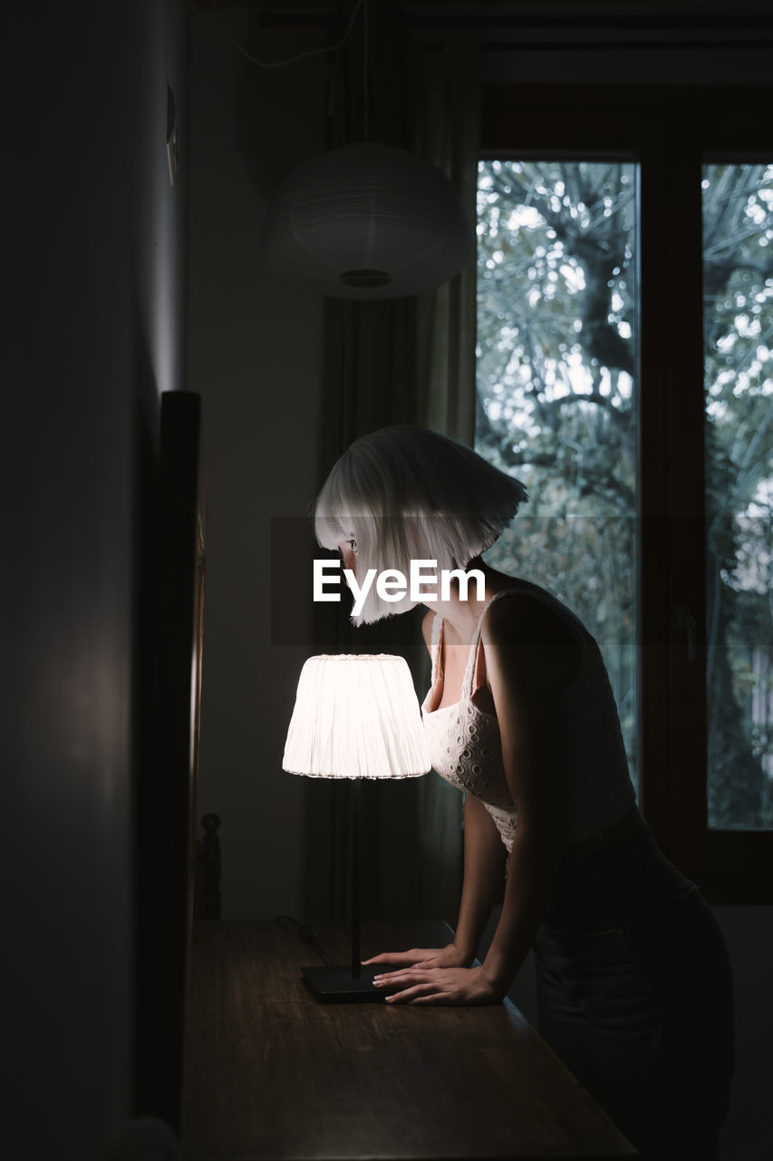 Young woman standing by illuminated lamp at home