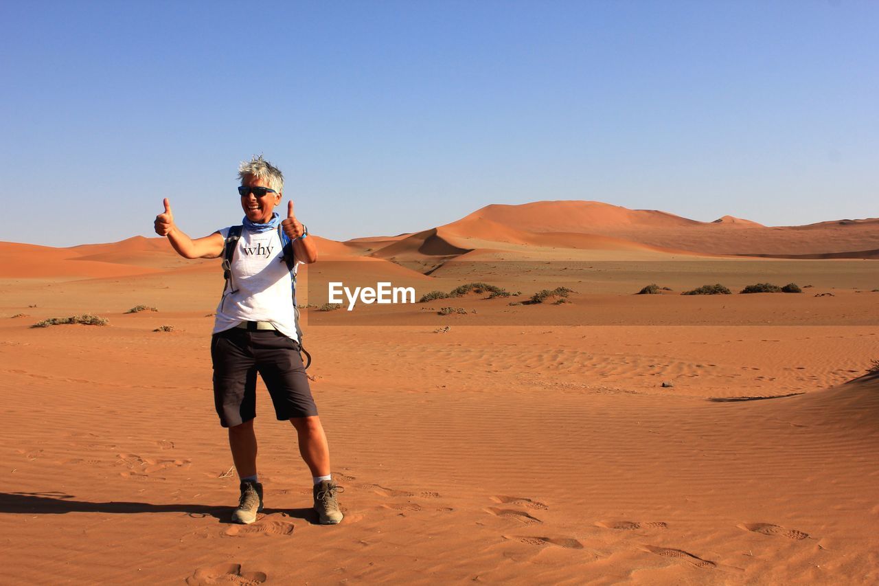 Full length of smiling woman gesturing while standing on sand dune