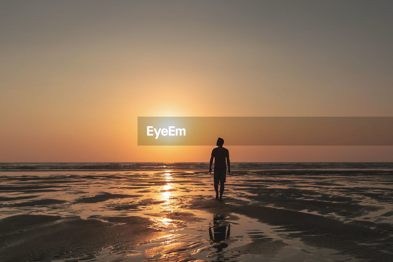 Silhouette man walking at beach against sky during sunset