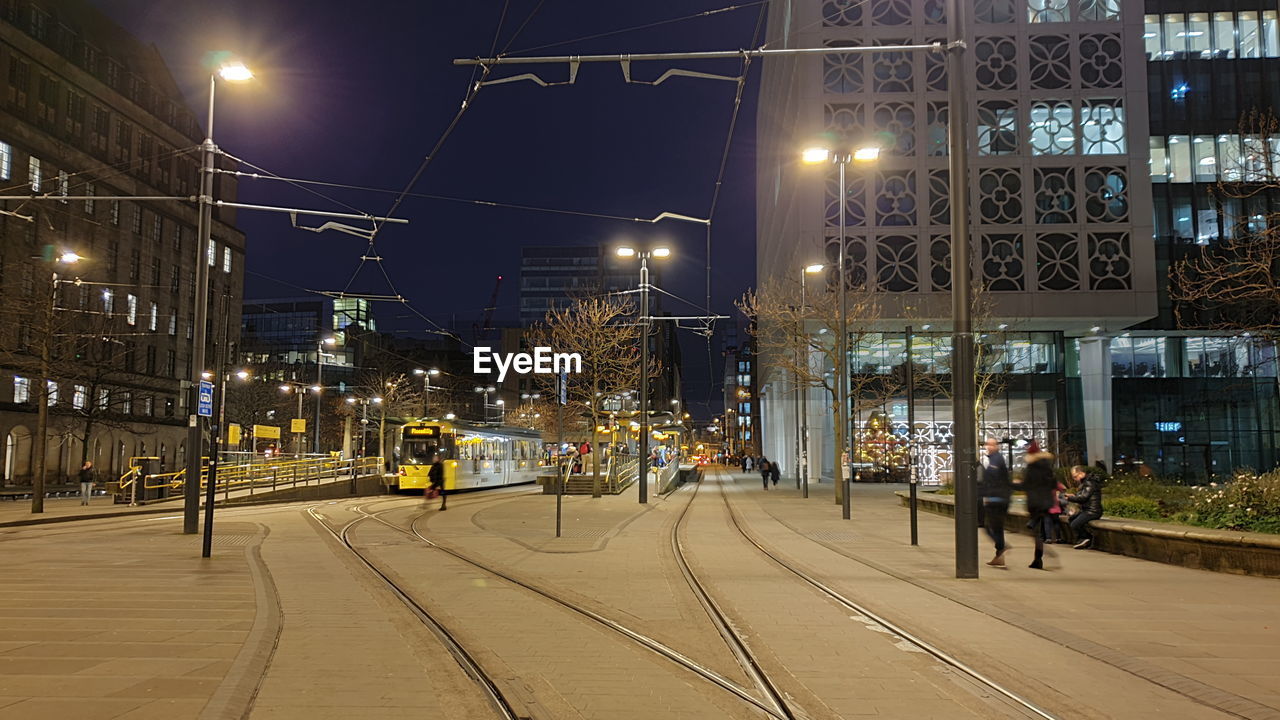 PEOPLE WALKING ON ILLUMINATED RAILROAD TRACKS AT NIGHT