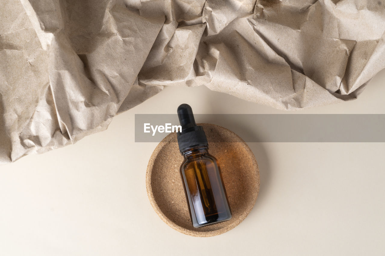 A face serum or oil in a brown dropper bottle lying on a beige craft paper background