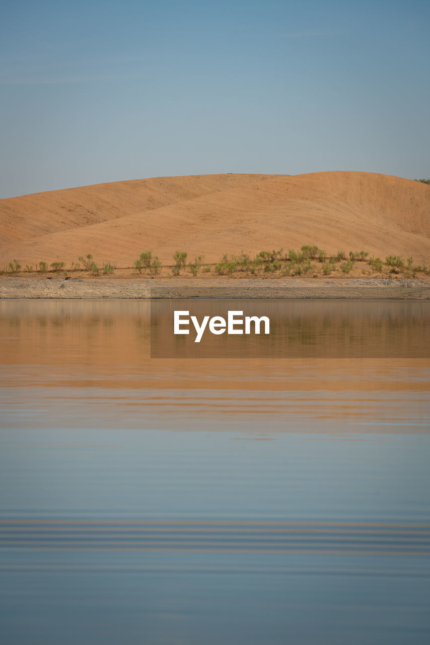 Desert like hill landscape with reflection on the water on a dam lake reservoir in terena, portugal