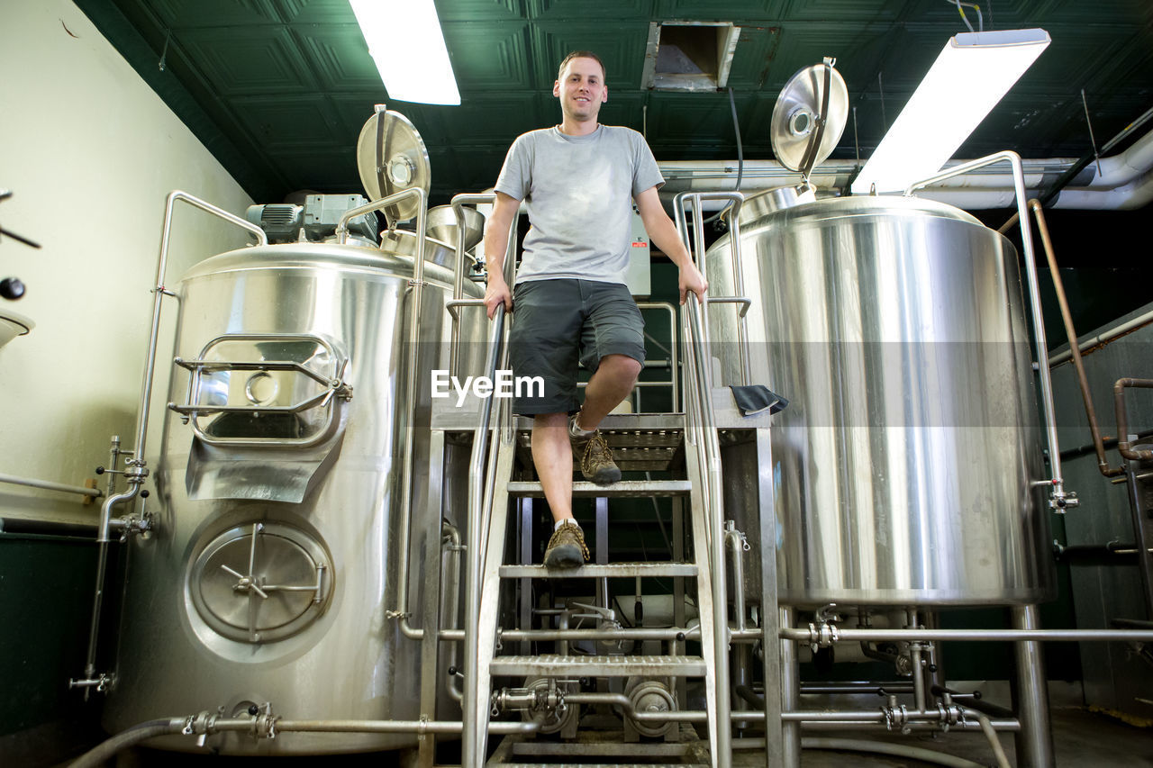 Low angle portrait of brewery worker standing by fermentation tanks
