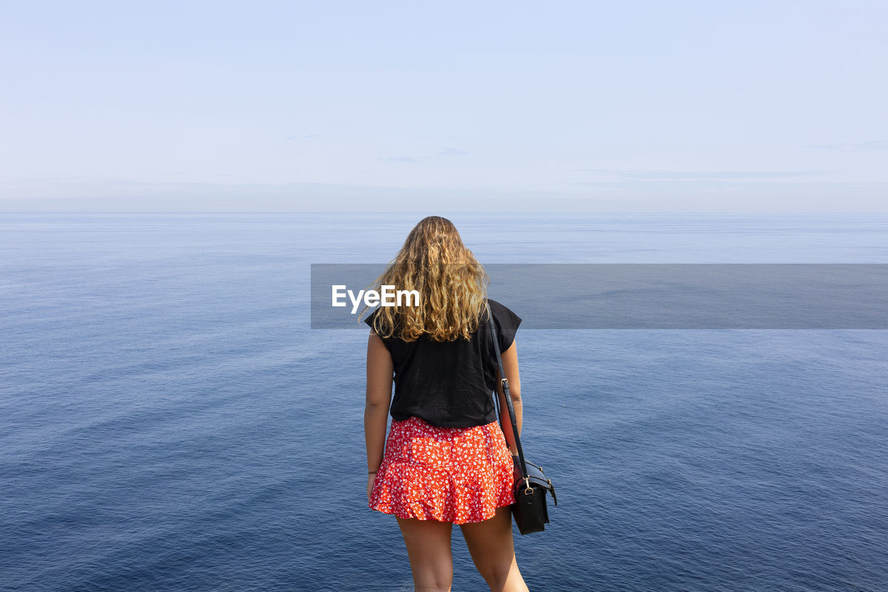 Back view of woman standing in front of the sea against sky