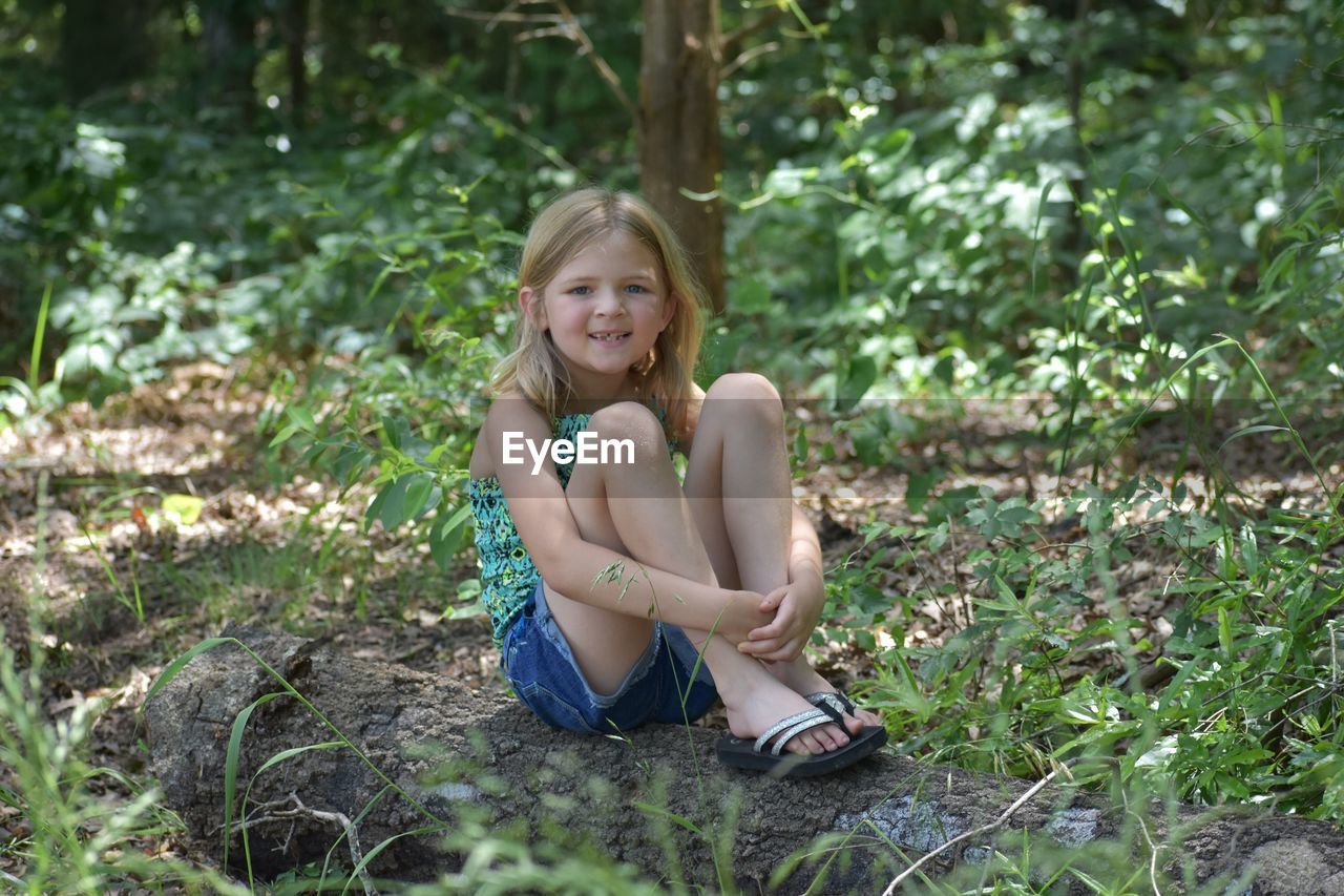 Portrait of smiling girl sitting on land in forest